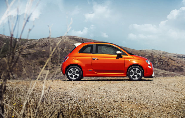 side view of electric orange Fiat 500e on the beac
